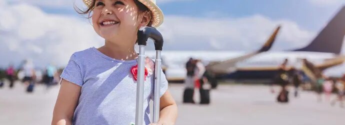 Une jeune fille souriante avec en arrière-plan une valise jaune avec des articles dont vous avez besoin pour des vacances en famille