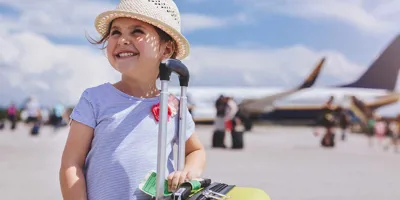 Une jeune fille souriante avec en arrière-plan une valise jaune avec des articles dont vous avez besoin pour des vacances en famille