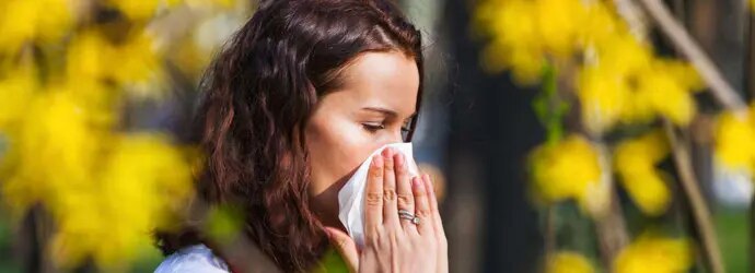 Une jeune femme éternue dans un mouchoir en papier dans un champ plein de fleurs sauvages avec un nombre élevé de pollen