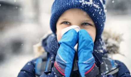 Un petit enfant vêtu de vêtements d'hiver se mouche le nez