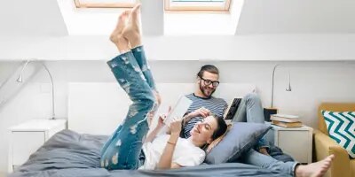 Un jeune couple assis sur un lit, lisent dans une chambre avec deux puits de lumière