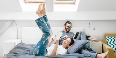 Un jeune couple assis sur un lit, lisent dans une chambre avec deux puits de lumière