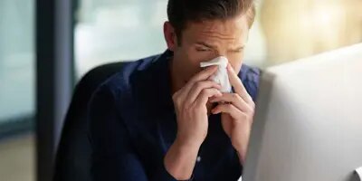 Un homme éternue vers son ordinateur, il est à la recherche de la période d'incubation du rhume