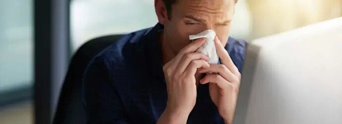 Un homme éternue vers son ordinateur, il est à la recherche de la période d'incubation du rhume