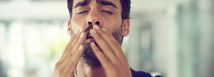 Un homme aux cheveux noir est sur le point d'éternuer et lève les mains vers son visage