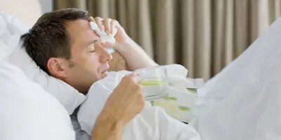 Un homme malade dans son lit tient une tasse de thé au citron et des mouchoirs