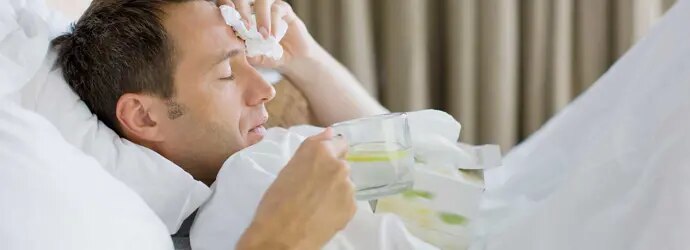 Un homme malade dans son lit tient une tasse de thé au citron et des mouchoirs