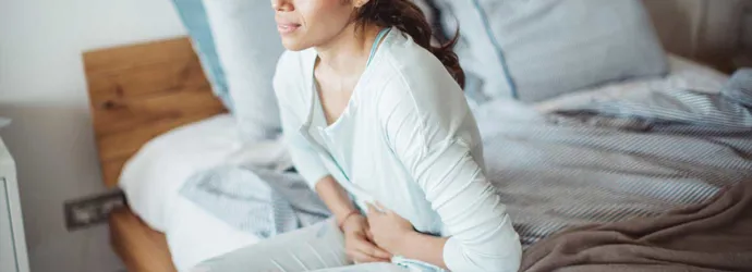 Nainen istuu sängyllä vatsakivuista kärsien