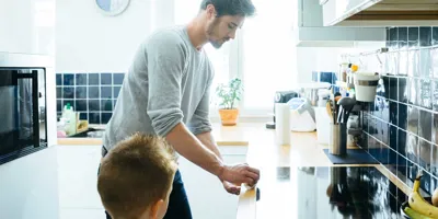 Mies puhdistaa keittiötasoa lapsen katsoessa tarkasti vierestä
