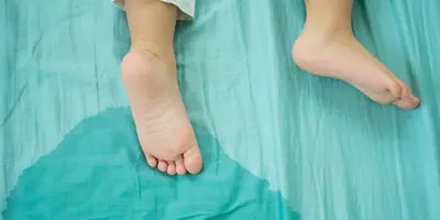 Lähikuva lapsen jaloista ja patjassa olevasta virtsasta