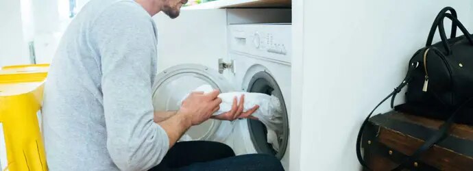Mies laittaa vaatteita pesukoneeseen