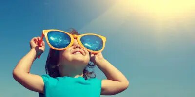 Un jeune enfant avec une paire de lunettes de soleil surdimensionnées et comiques fait le plein de vitamine D grâce au soleil dans le ciel