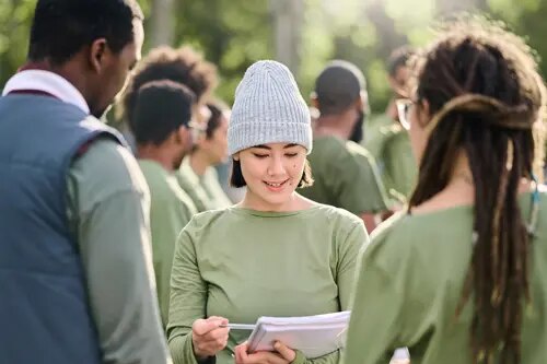 Une femme souriante, en plein air, lit un document à deux autres personnes.