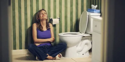 Femme assise par terre à côté des toilettes, se tenant le ventre de douleur