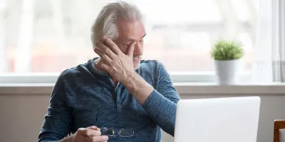 Un homme âgé devant un ordinateur portable a des démangeaisons dans l'oeil