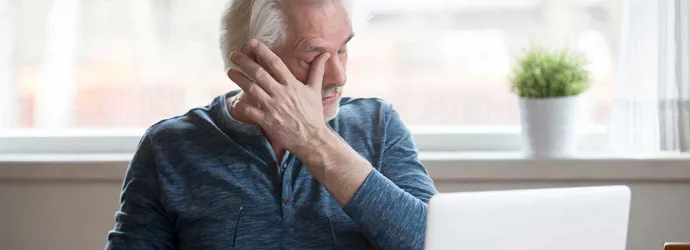Un homme âgé devant un ordinateur portable a des démangeaisons dans l'oeil