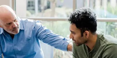 Un homme âgé, la main sur l'épaule, conseille un jeune homme.