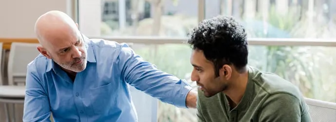 Un homme âgé, la main sur l'épaule, conseille un jeune homme.