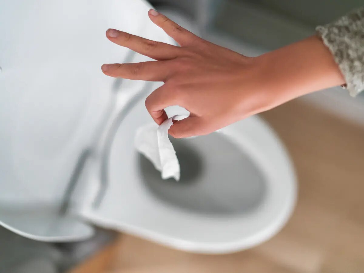 Photo d’une main qui jette du papier toilette humide dans les toilettes.