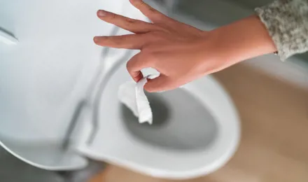 Photo d’une main qui jette du papier toilette humide dans les toilettes.