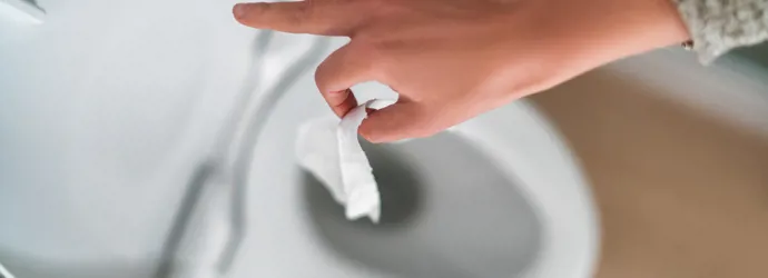 Photo d’une main qui jette du papier toilette humide dans les toilettes.
