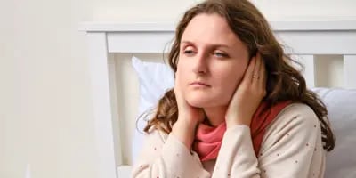 Femme malade assise sur un lit, ayant ses mains sur ses oreilles