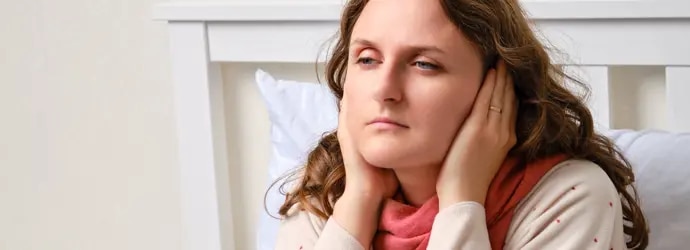 Femme malade assise sur un lit, ayant ses mains sur ses oreilles
