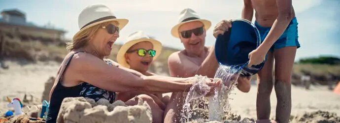Deux enfants et leurs grands-parents à la plage, construisant un château de sable