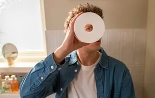 Image d’un homme dans sa salle de bain tenant un rouleau de papier toilette et regardant au centre.