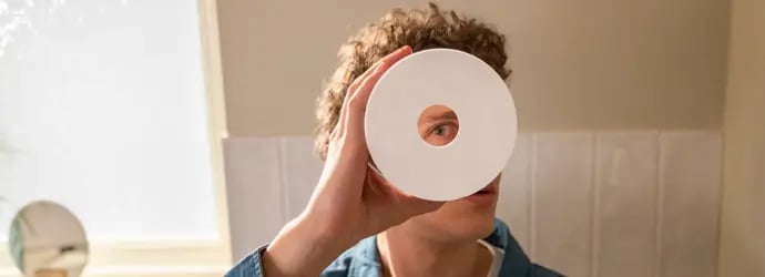 Image d’un jeune homme tenant un rouleau de papier toilette devant son œil et regardant à travers le trou.