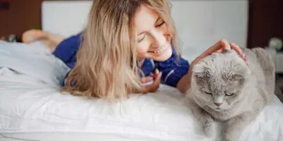Une femme allongée sur son lit, caresse son chat, elle ne présente pas clairement les symptômes d'allergie aux poils de chat