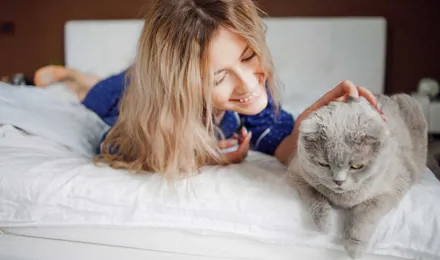 Une femme allongée sur son lit, caresse son chat, elle ne présente pas clairement les symptômes d'allergie aux poils de chat