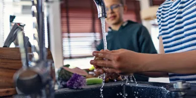 Des garçons rincent des légumes frais sous le robinet dans une cuisine moderne.