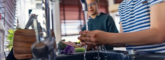 Des garçons rincent des légumes frais sous le robinet dans une cuisine moderne.