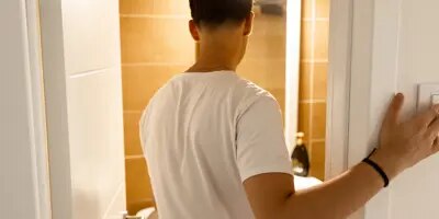 Homme en chemise blanche éteignant les lumières dans une pièce carrelée.