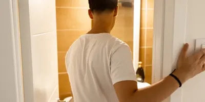 Homme en chemise blanche éteignant les lumières dans une pièce carrelée.