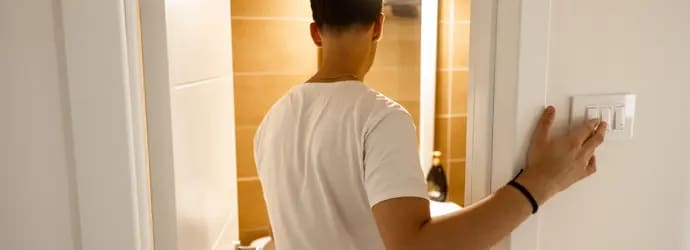 Homme en chemise blanche éteignant les lumières dans une pièce carrelée.