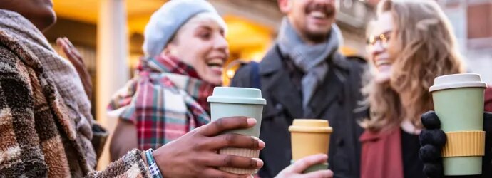 Des amis rieurs tiennent des tasses de café à l'extérieur.