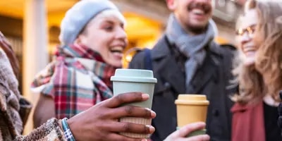 Des amis rieurs tiennent des tasses de café à l'extérieur.