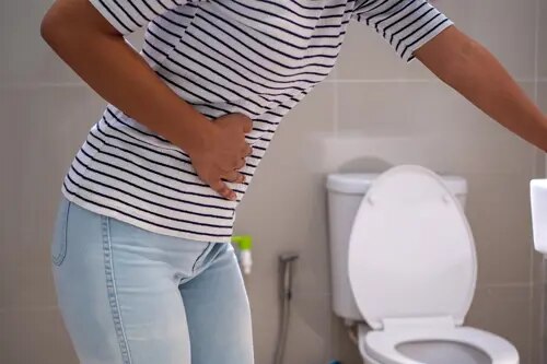 Une personne se tient la région abdominale alors qu'elle se trouve près des toilettes.