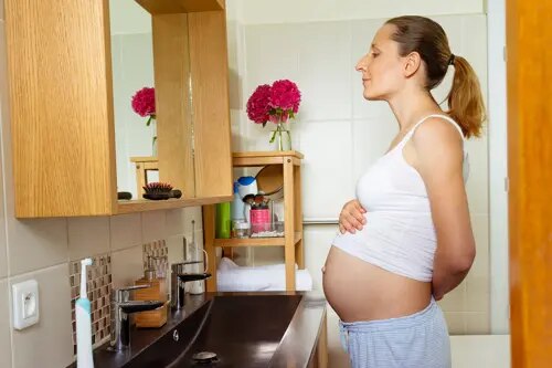 Une femme enceinte se tient devant un miroir, son haut relevé sur sa bosse de grossesse.