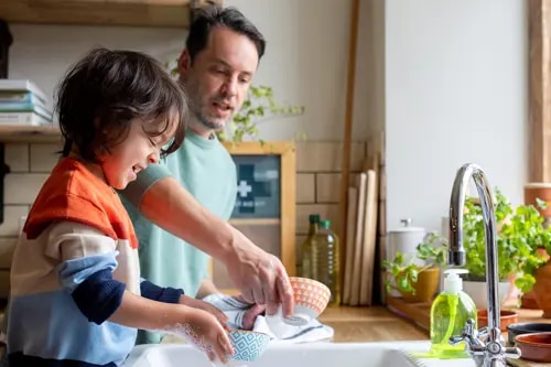 Un garçon et un homme souriants font la vaisselle.