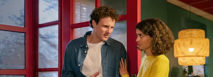 Un homme et une femme se tiennent devant la porte d'un restaurant, l'homme se tient le ventre.