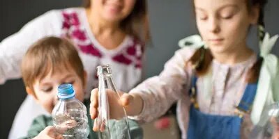 Une jeune famille souriante trie des bouteilles en plastique et en verre pour les recycler.