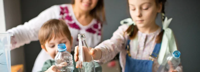 Une jeune famille souriante trie des bouteilles en plastique et en verre pour les recycler.