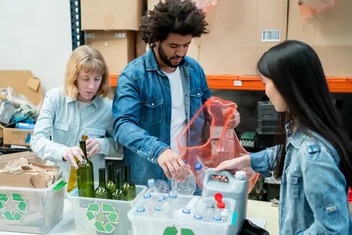 Trois personnes trient le carton, le verre et le plastique dans des conteneurs séparés.